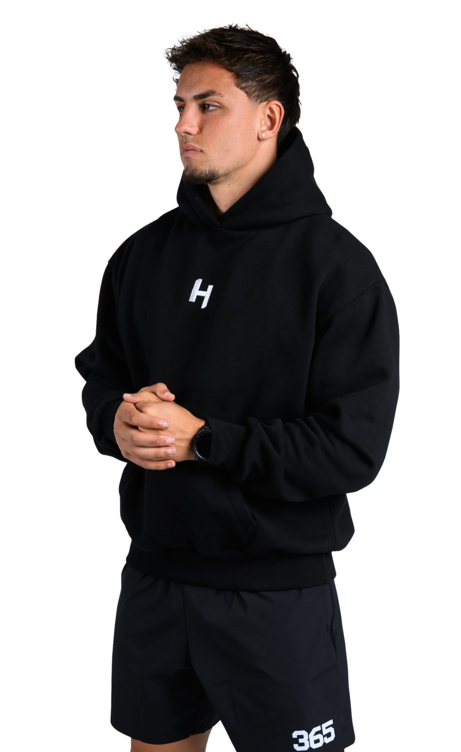 Person wearing a black hoodie and shorts with a visible brand logo on a white background