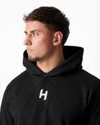 Man wearing a black hoodie with a white logo on a plain background