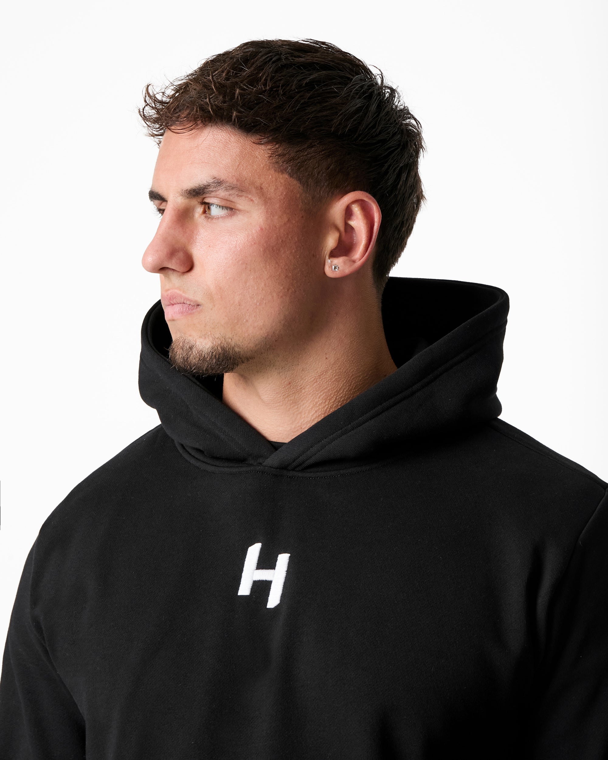 Man wearing a black hoodie with a white logo on a plain background