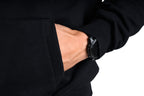 Person wearing a black jacket with a watch on the wrist against a white background