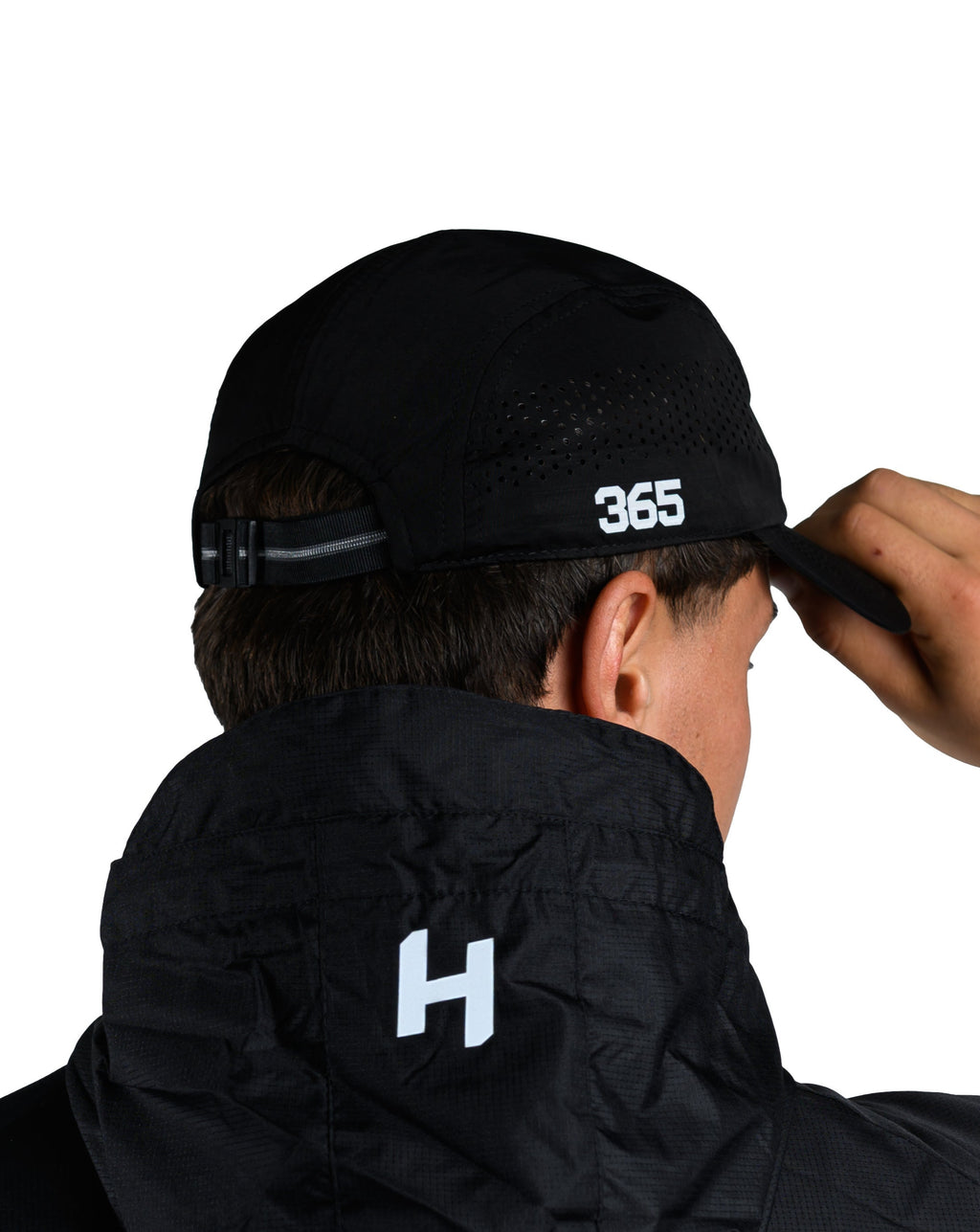 Person wearing a black jacket with '365' printed on the back, adjusting a black cap.