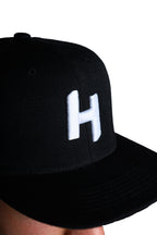 Black cap with a white 'H' logo on a white background