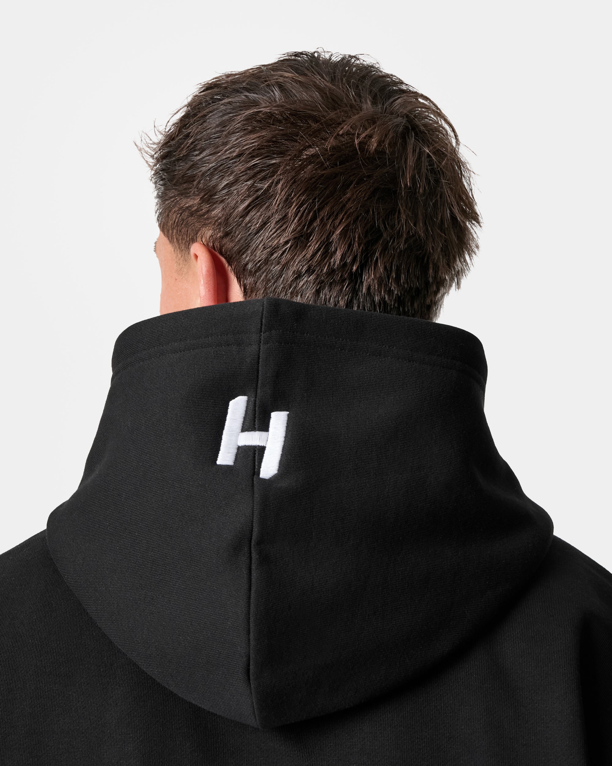 Person wearing a black hoodie with a white logo on the hood against a light gray background